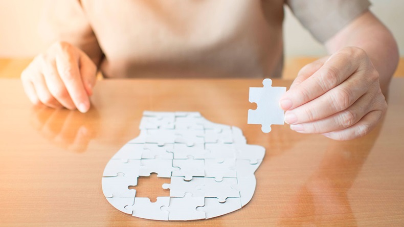 Elderly woman hands holding missing white jigsaw puzzle piece down into the place as a human head brain shape. Creative idea for memory loss, dementia, Alzheimer's disease and mental health concept.