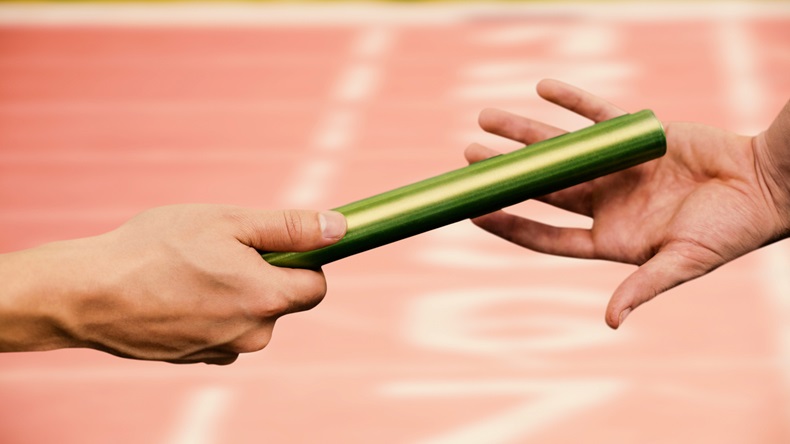 Man passing the baton to partner on track against close up of the track starting point - Image 