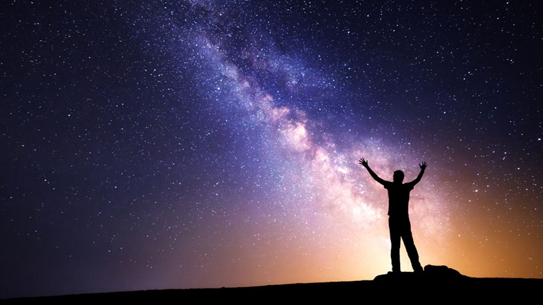 Milky Way. Night sky with stars and silhouette of a man with raised-up arms. 