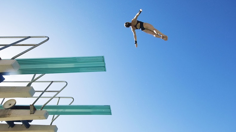 Low angle view of a female swimmer preparing to dive from diving board against clear blue sky