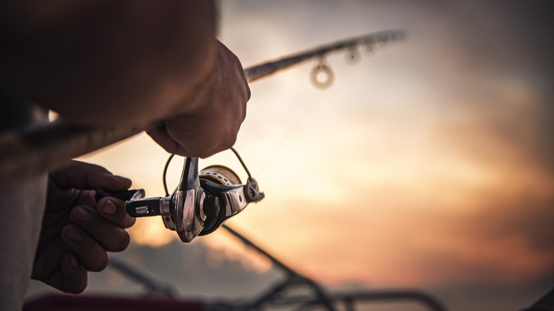 Fishing rod wheel closeup, man fishing with a beautiful sunrise behind him
