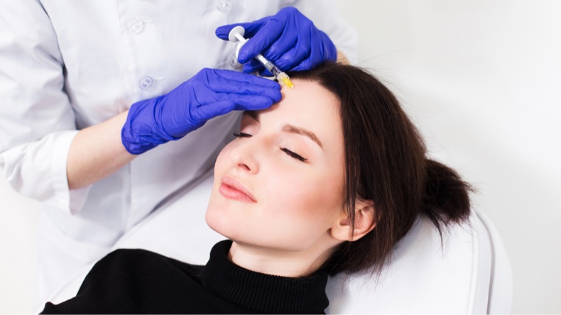 Close up of hands of cosmetologist making botox injection in female face