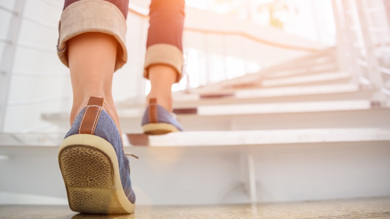 Young adult woman walking up the stairs with sun sport background.