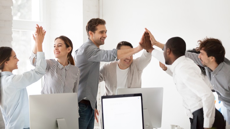 Excited multiracial colleagues celebrating team victory giving high five in office, happy employees group join hands together promising loyalty engagement, expressing trust unity support in teamwork