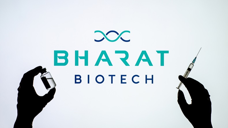 Backlit single shot image of Bharat Biotech logo on tv screen with a hand holding an Covid-19 vaccine concept
