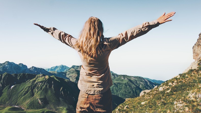 Happy Woman traveler over mountains raised hands