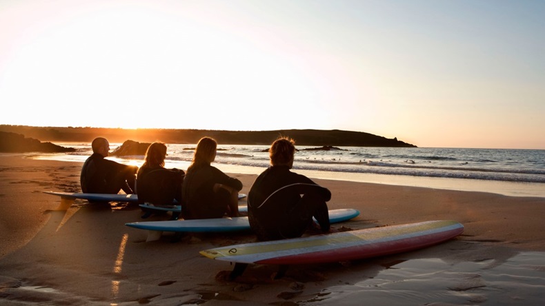 Four people sitting on the beach with surfboards