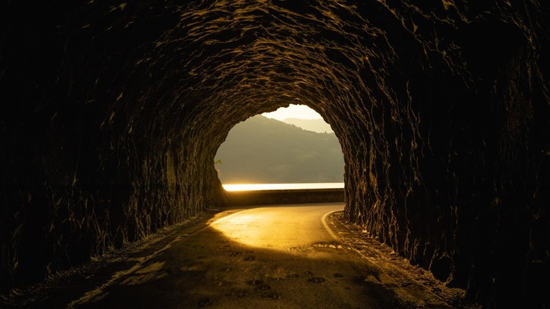 Dark tunnel with a road winding through to a light at the end