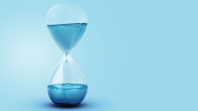 Hourglass filled with water against blue background, concept of time passing