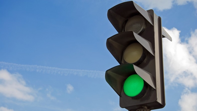 Set of traffic lights against a bright blue sky, green light illuminated