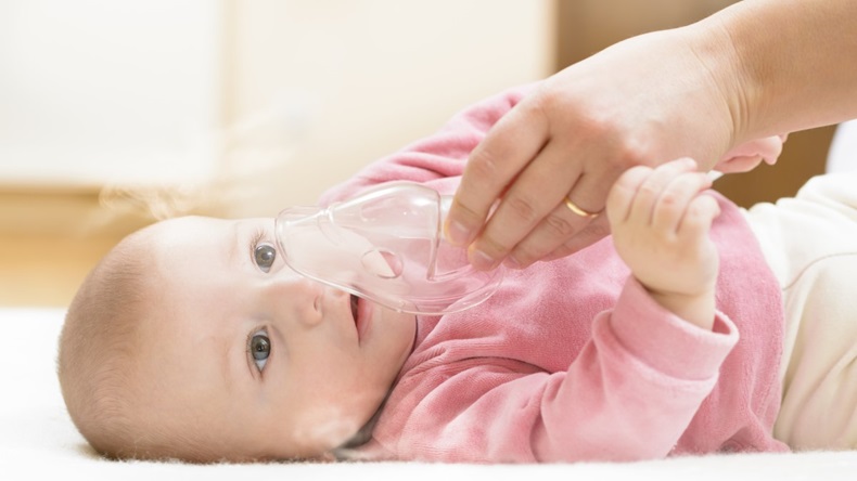 hand putting oxygen mask on baby lying down