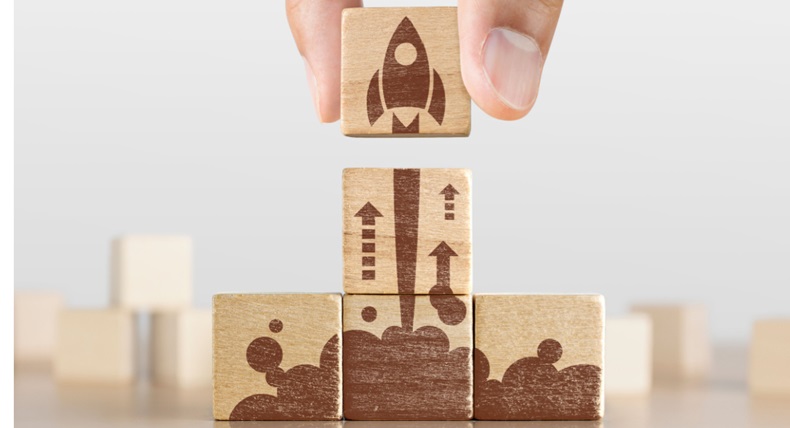 Wooden blocks with launching rocket graphic arranged in pyramid shape and a man is holding the top one.