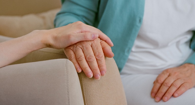 Caregiver cheers up senior lady patient touching hand while sits in armchairs in light room