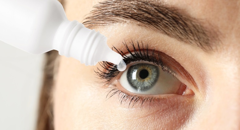 Woman applying eye drops on light background, closeup